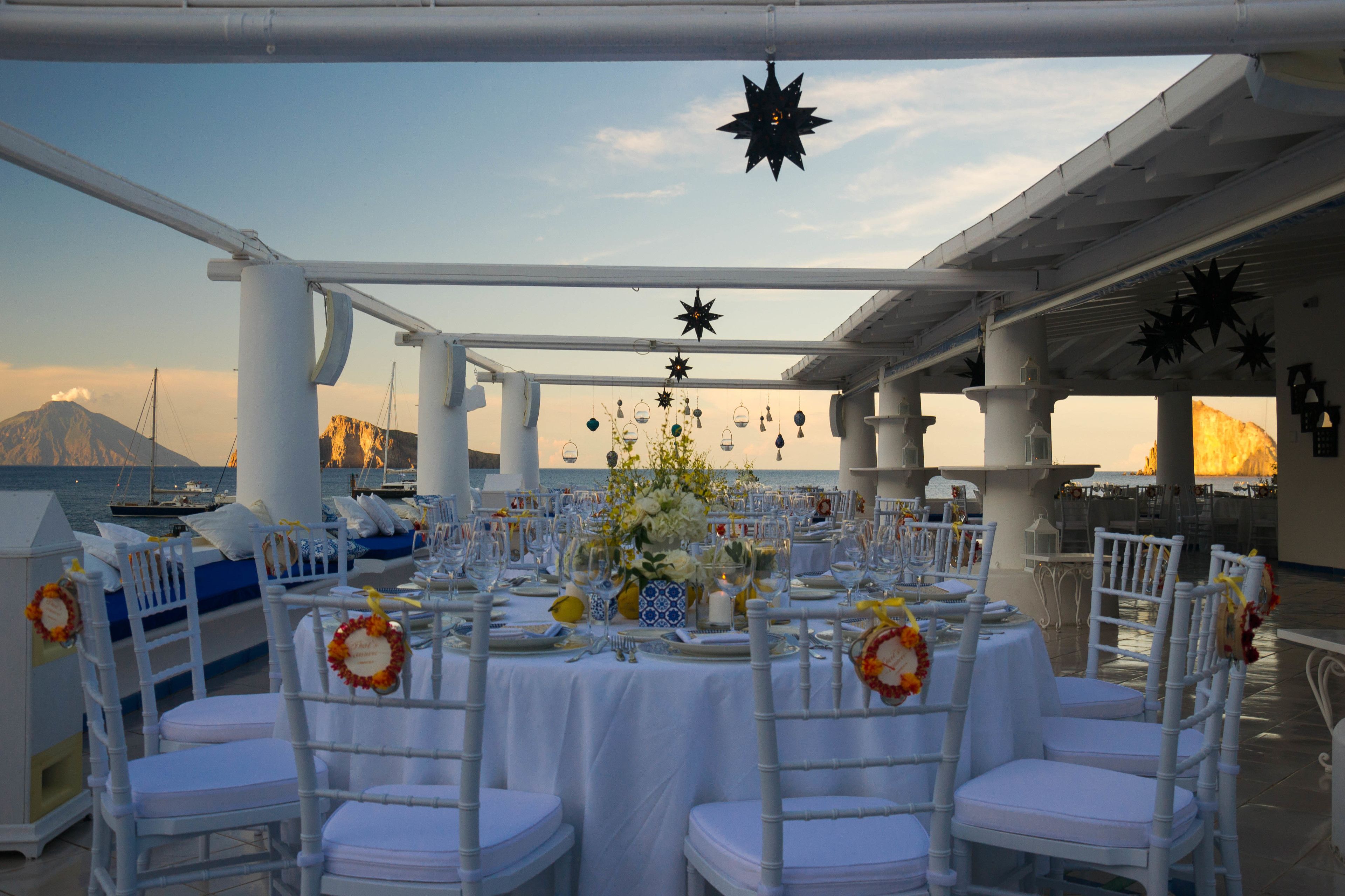 Un espace de restauration en plein air avec des tables et des chaises blanches, décoré de fleurs et d’ornements en forme d’étoile.