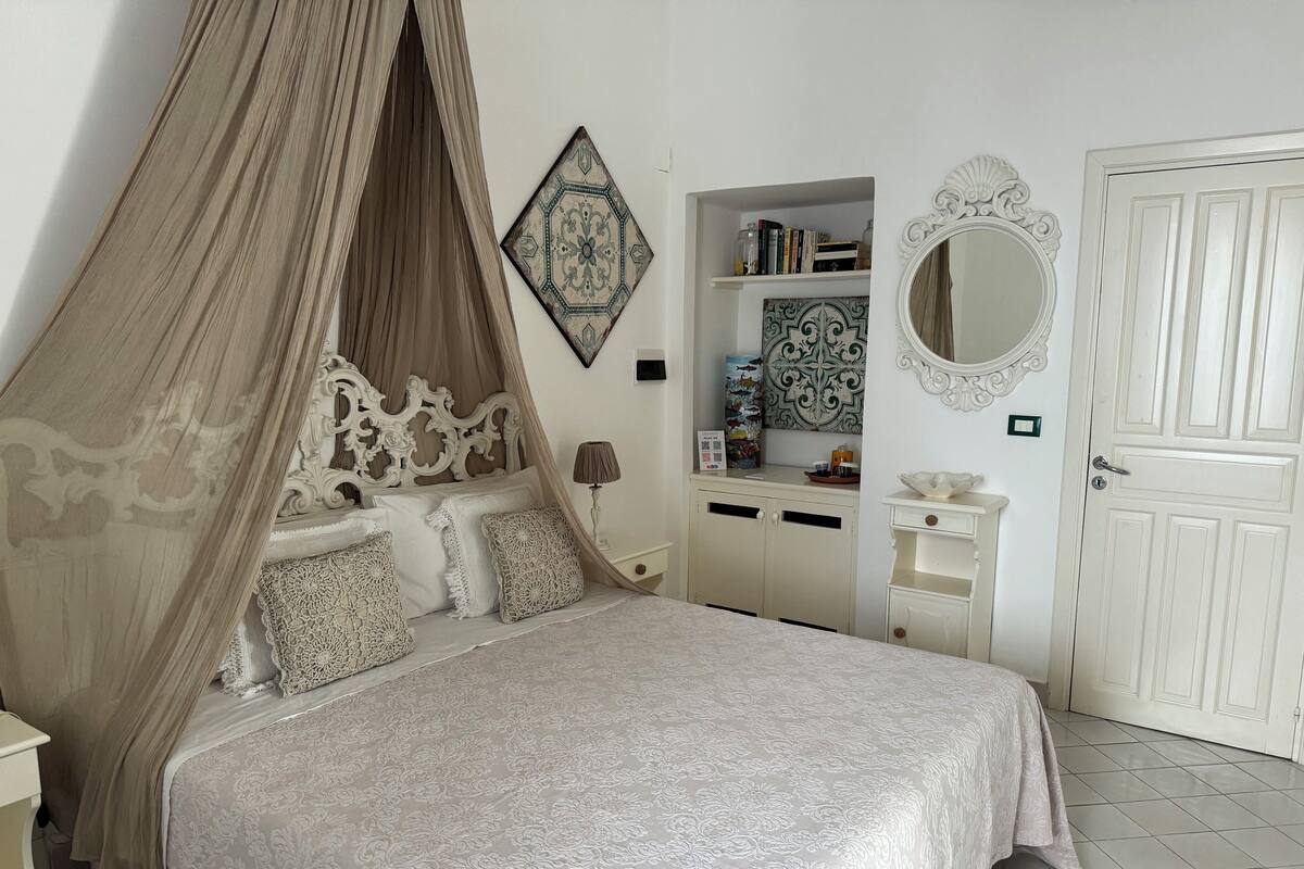 Ein Schlafzimmer mit Himmelbett, Nachttisch, Kommode, Spiegel und einer Tür.
