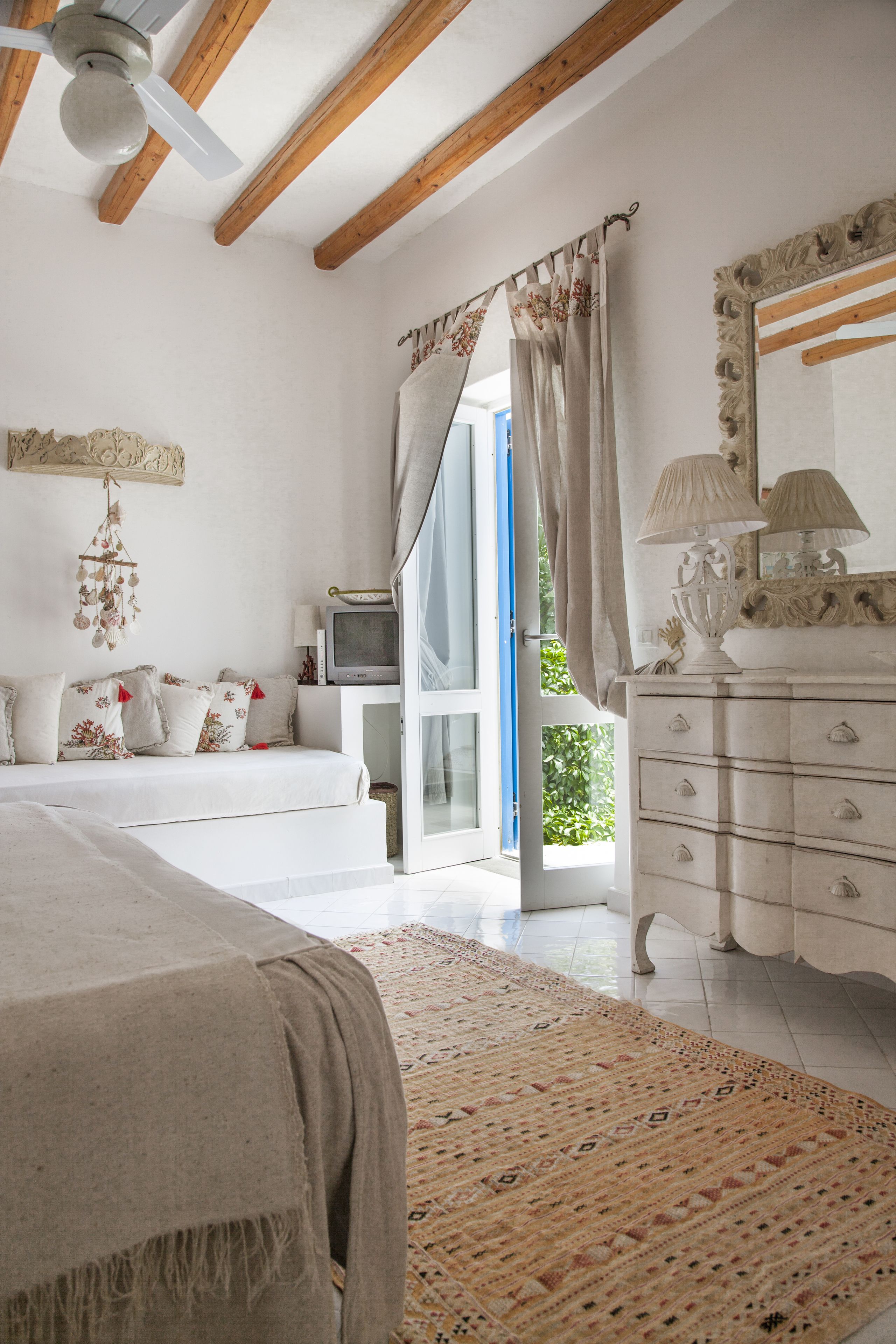 A bedroom with a bed, a dresser, a television, and a window with curtains.
