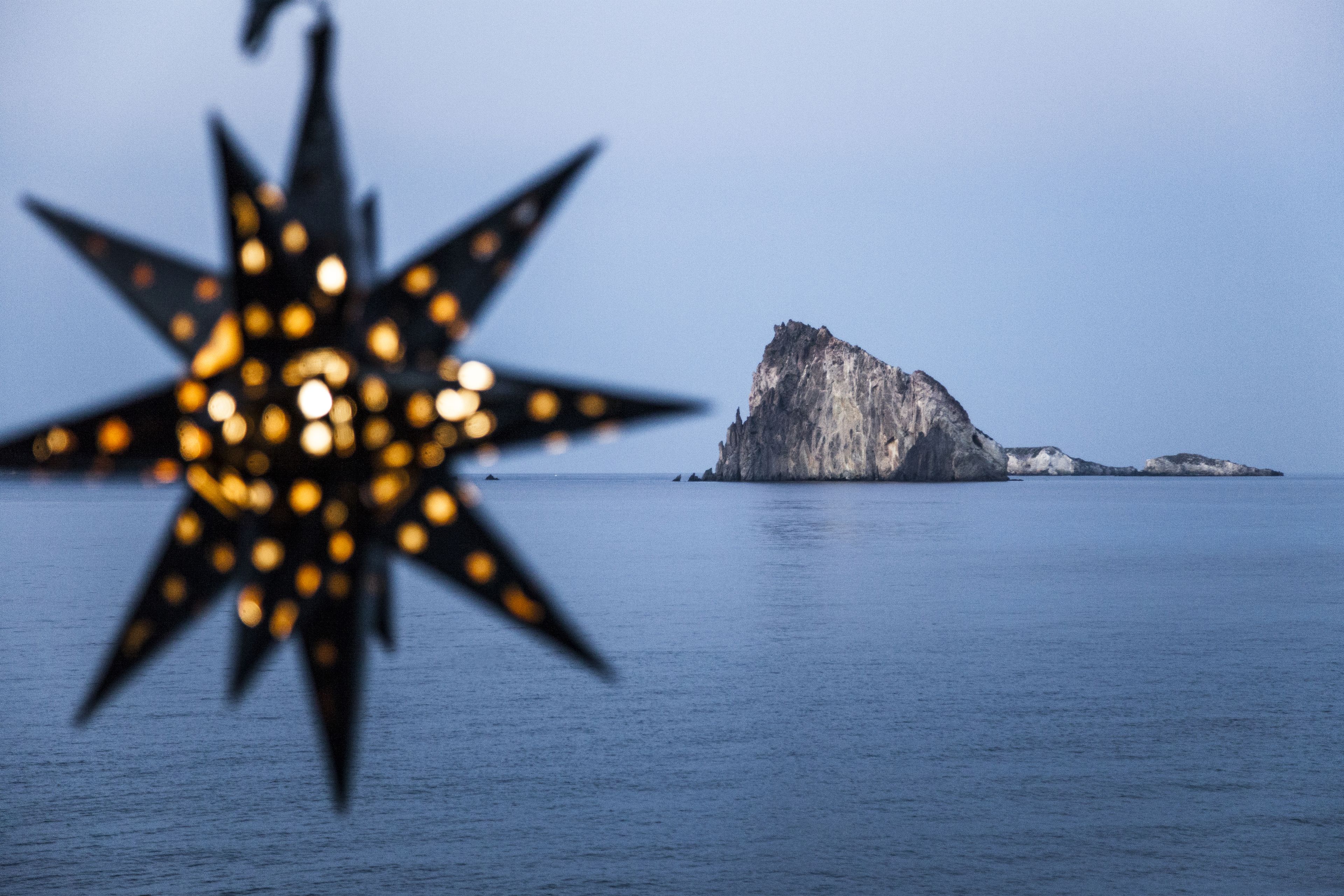 Un luminaire en forme d’étoile au premier plan, avec une île rocheuse en arrière-plan.