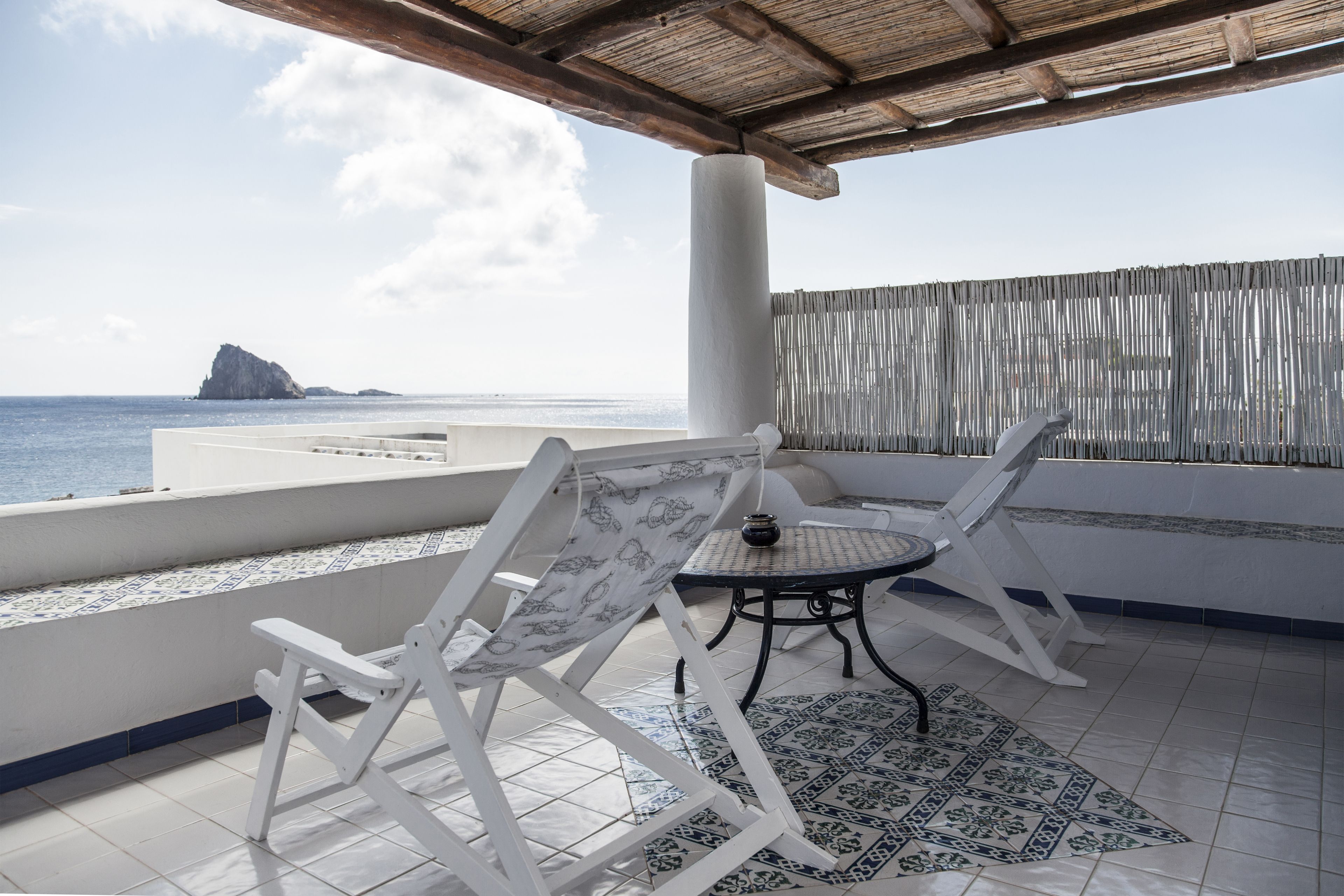 Una terraza con dos sillas blancas plegables y una pequeña mesa redonda, con vistas al mar.