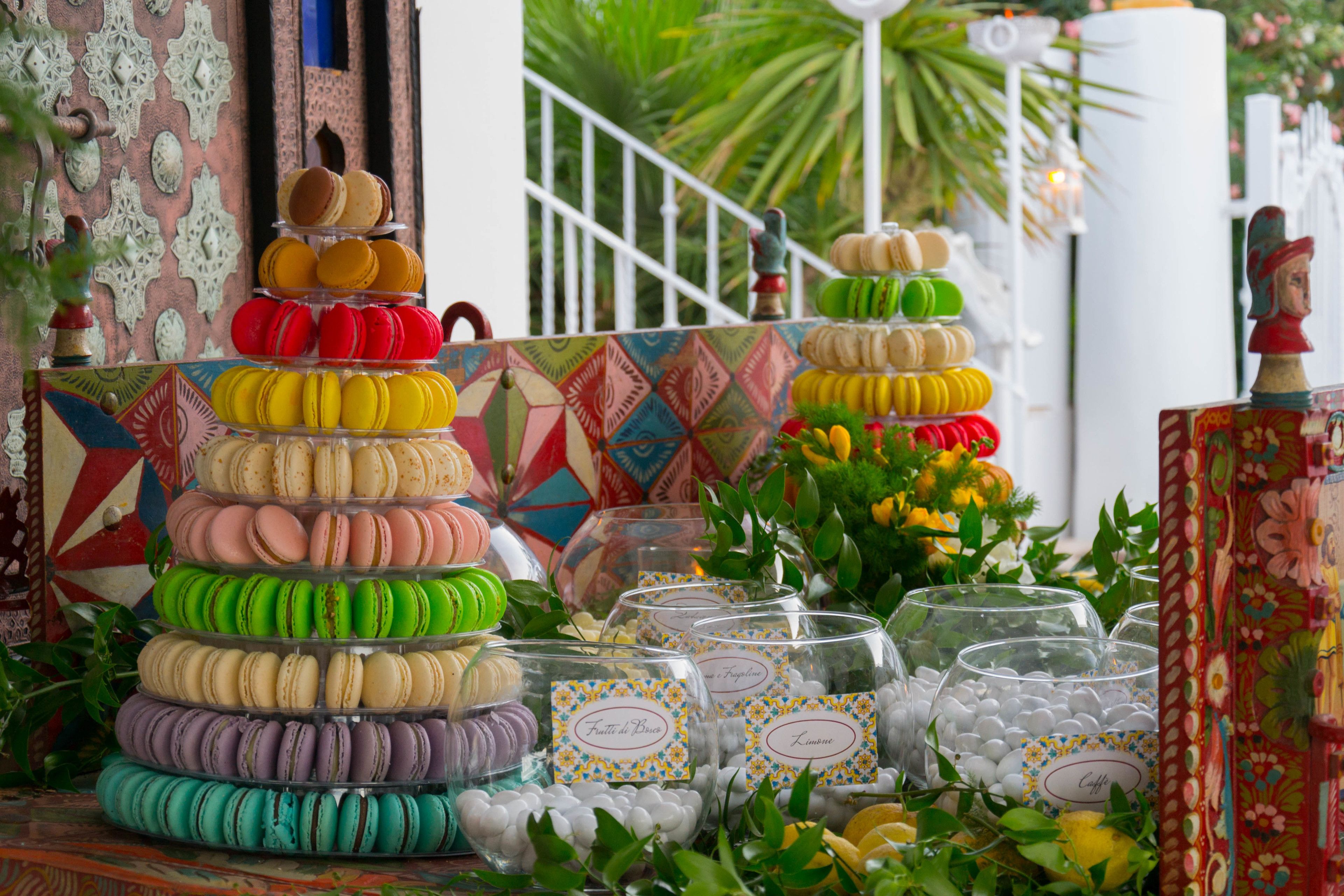 A display of colorful macarons arranged in a pyramid, surrounded by glass jars with labels.