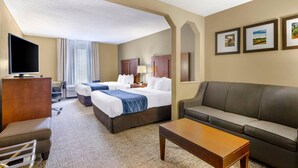 A hotel room with two beds, a sofa, a TV, and a desk.
