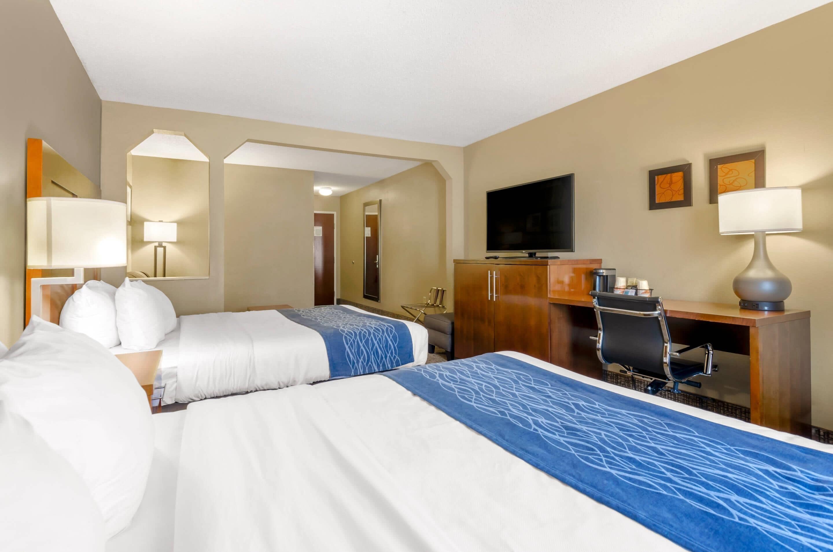 Una habitación de hotel con dos camas, un escritorio, un televisor y un espejo.