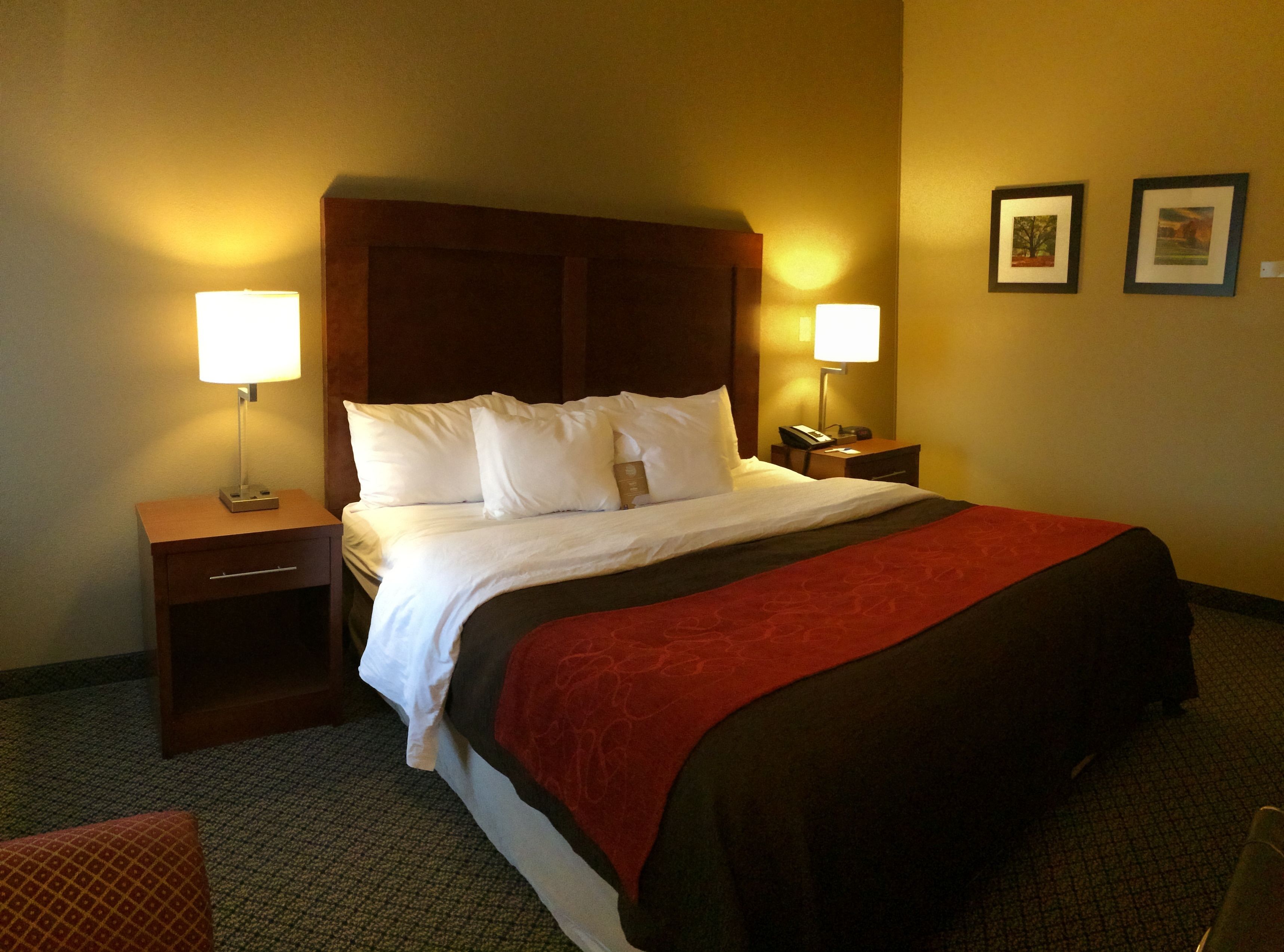 Habitación de hotel con una cama grande, dos mesitas de noche, una lámpara de noche y una manta roja.