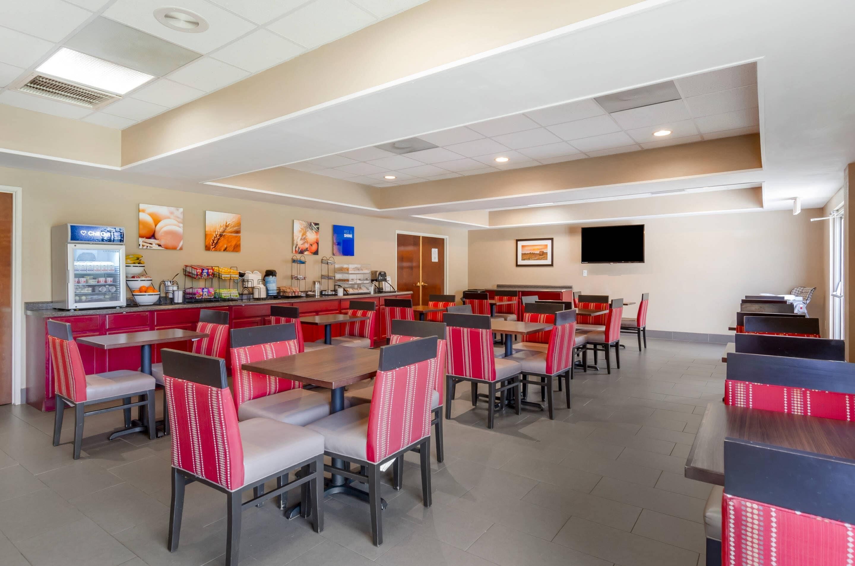 A spacious dining area with multiple tables and chairs, a self-service beverage station, and a flat-screen TV mounted on the wall.
