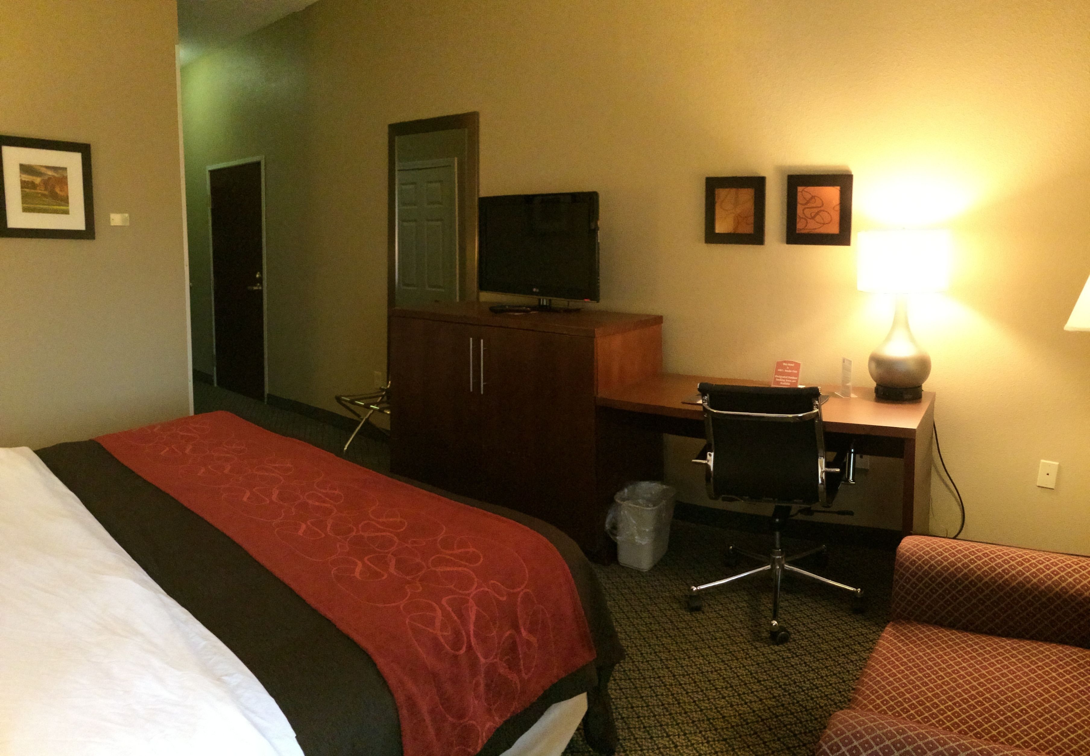A hotel room with a bed, desk, chair, and a TV.