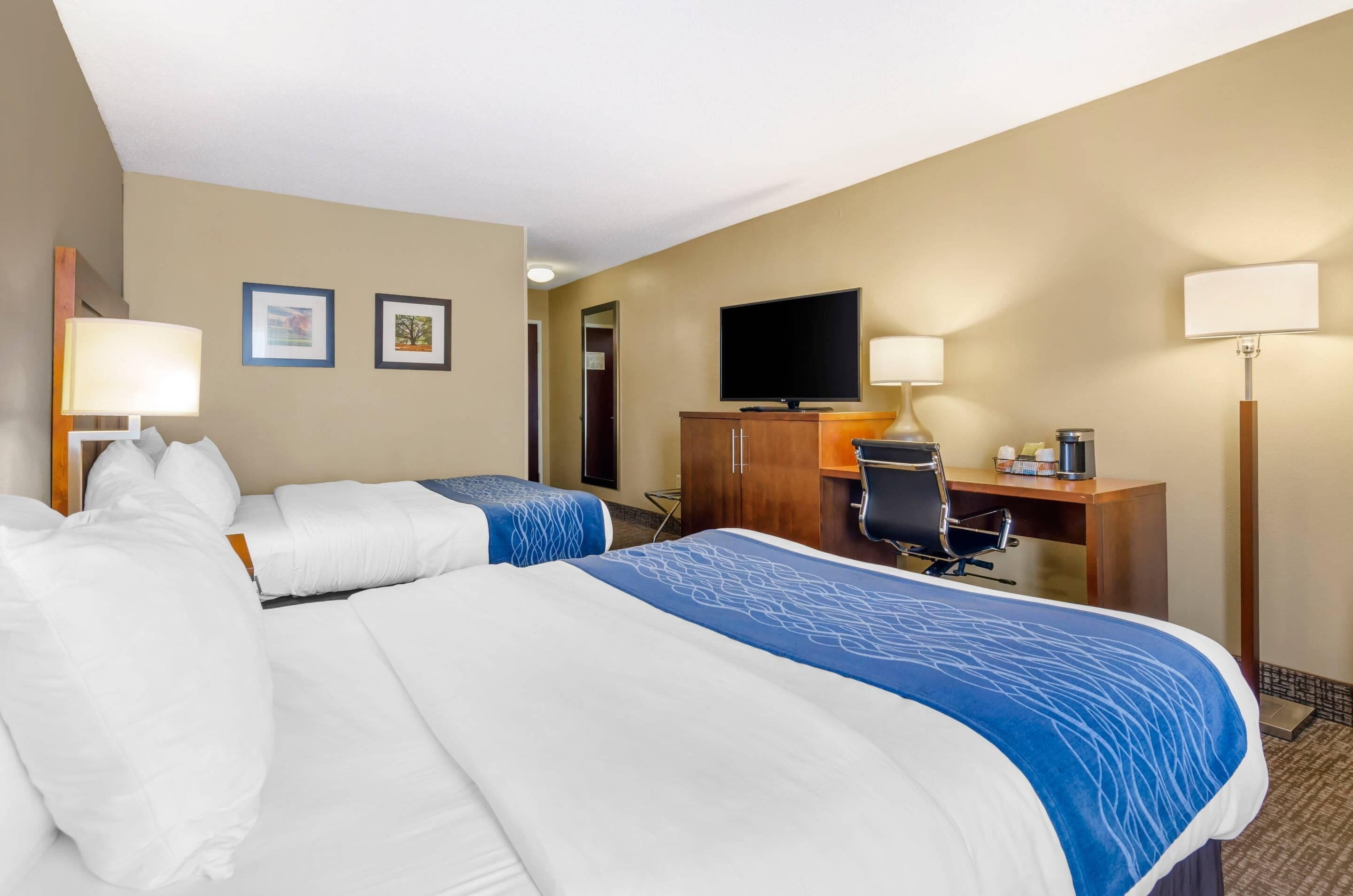 A hotel room with two beds, a desk, a television, and a lamp.