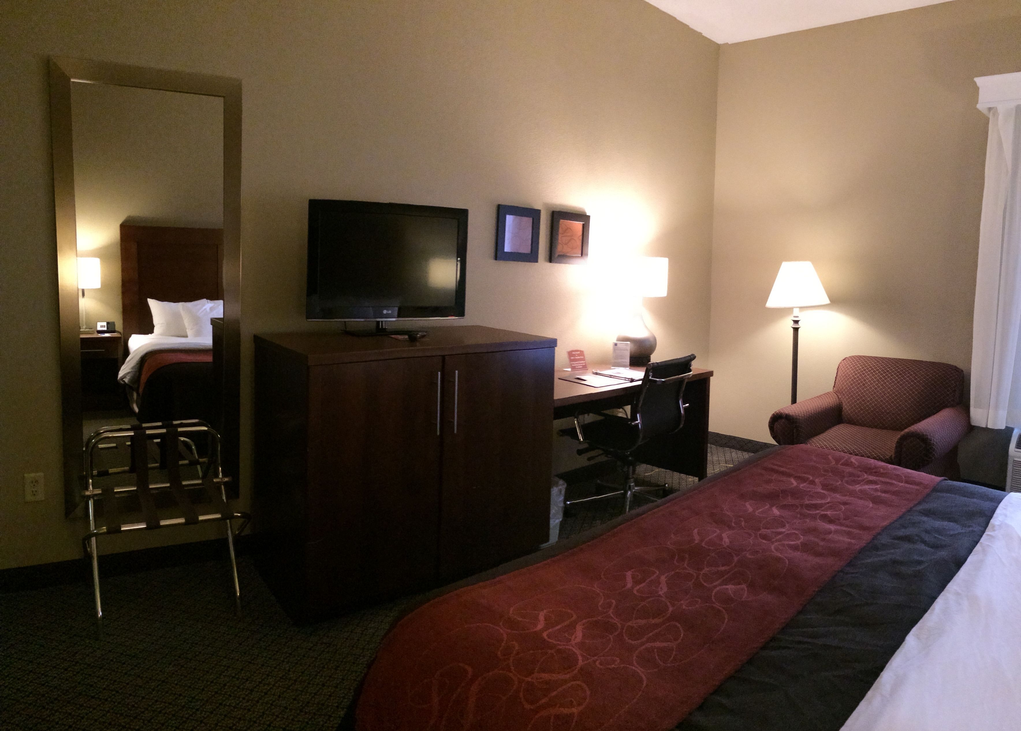 A hotel room with a bed, a desk, a chair, a television, and a mirror.