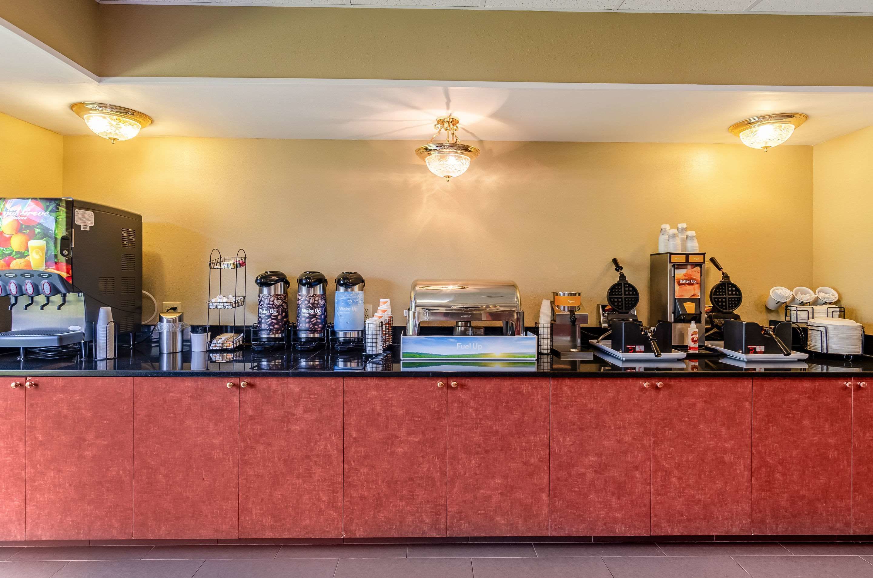 A hotel reception area with a coffee station, a waffle maker, and a refrigerator.