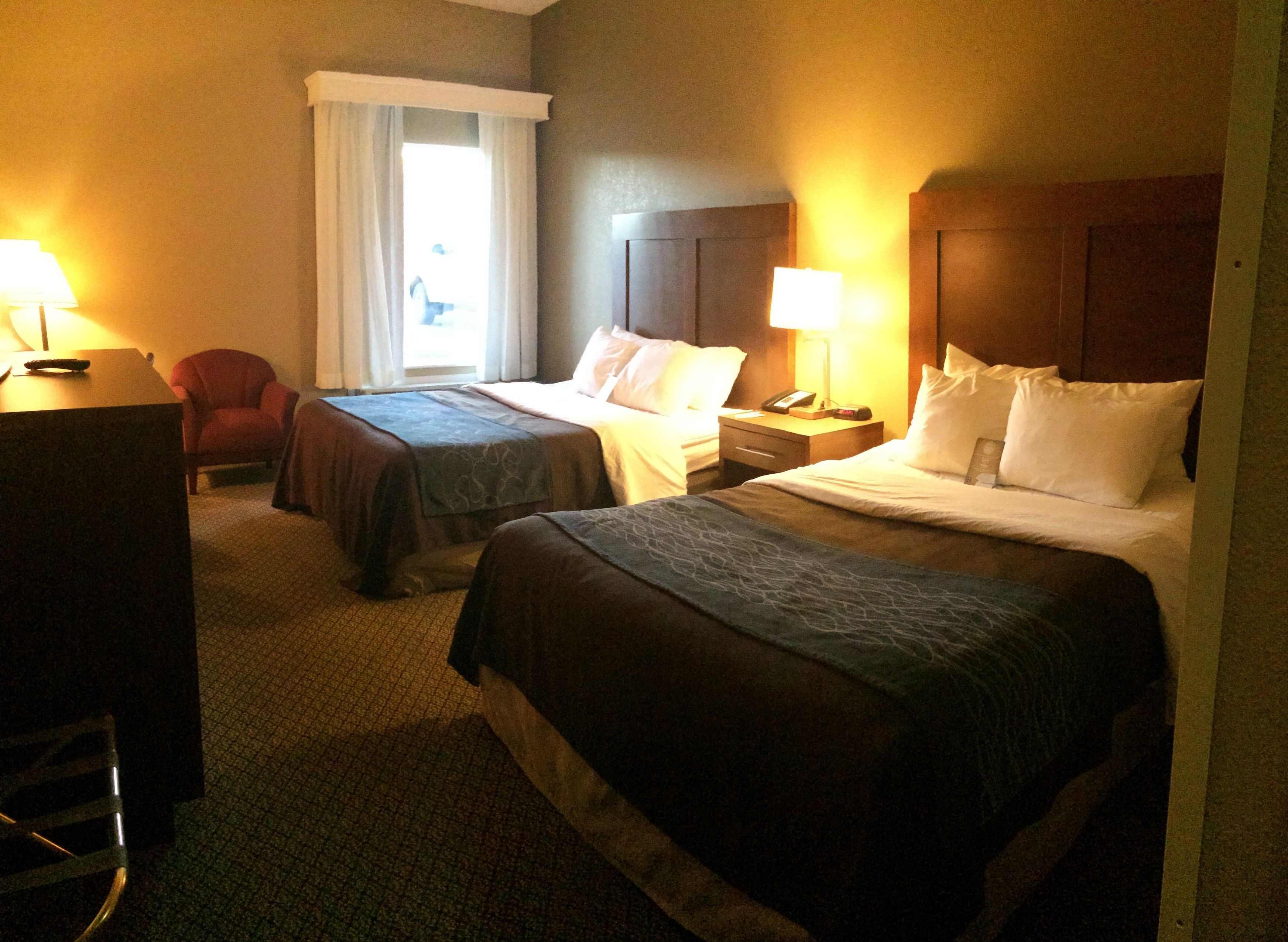 Ett hotellrum med två sängar, ett skrivbord, en stol och ett fönster med gardiner.