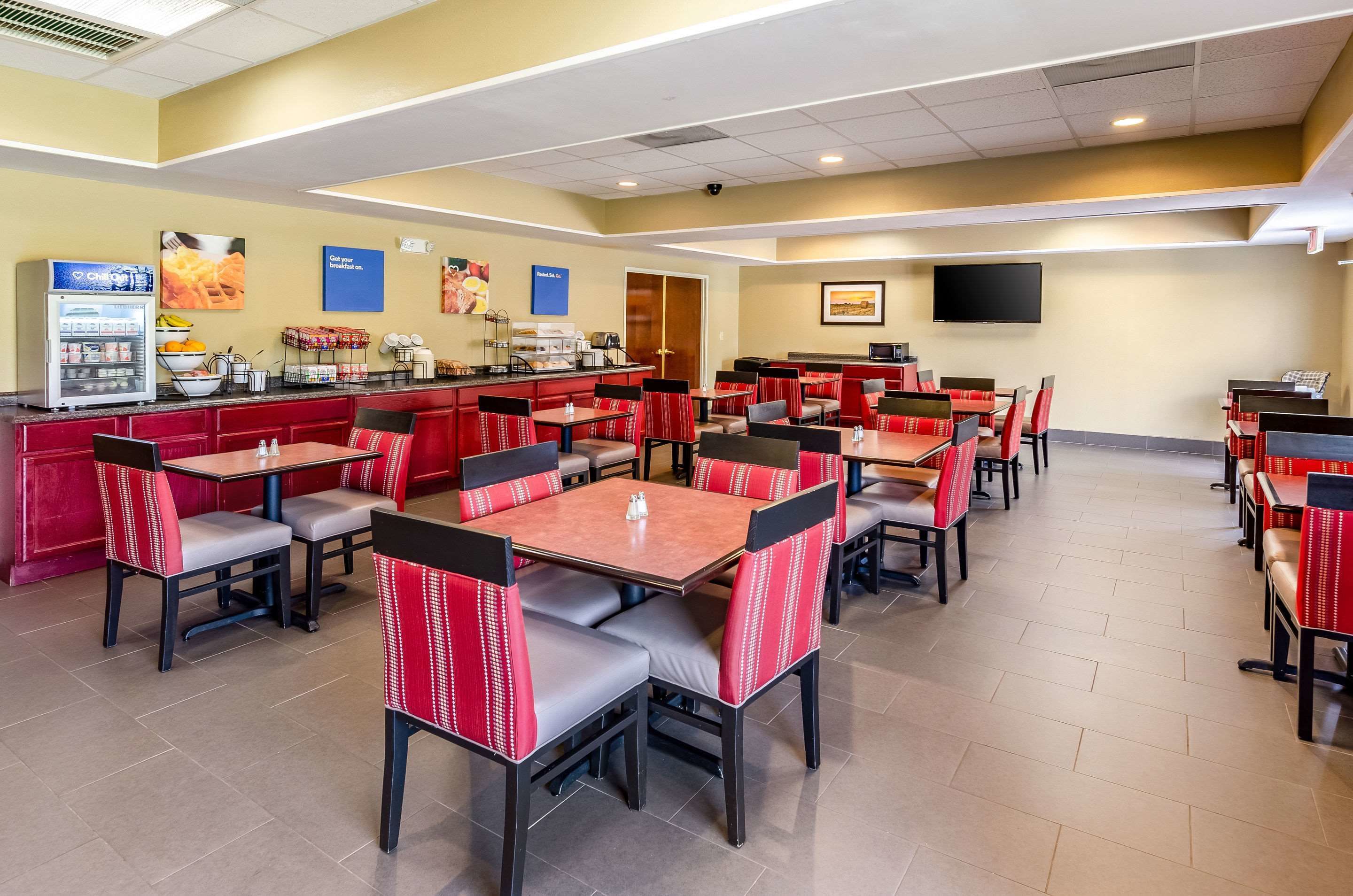 Zona de dinar d'hotel amb diverses taules i seients, una estació d'auto-servei per a begudes i un televisió de pantalla plana penjada a la paret.