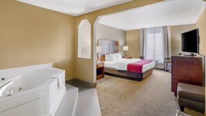 A hotel room with a large bed, a separate bathroom with a bathtub, a desk, and a television.