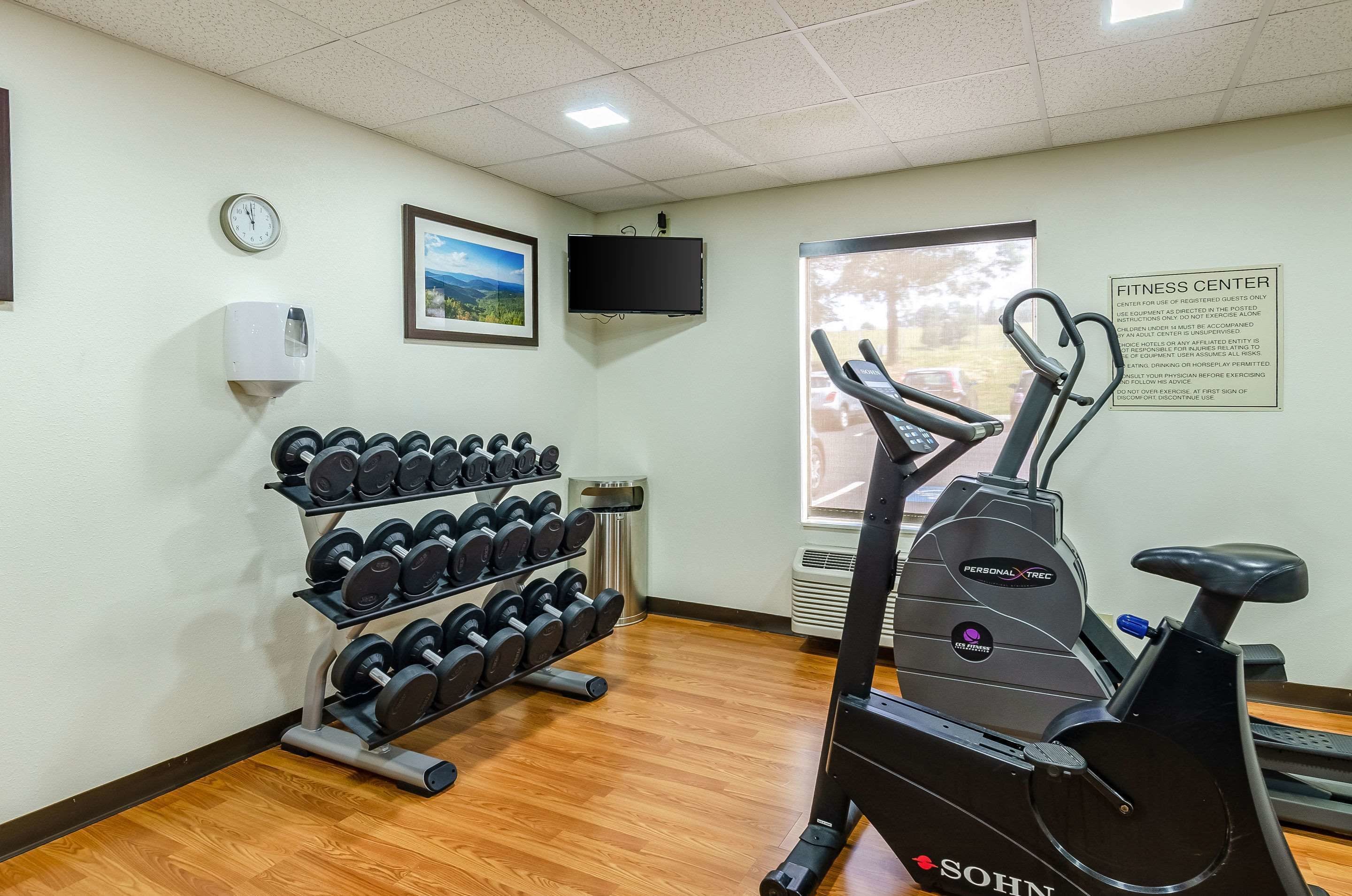 Una palestra con tapis roulant, pesi, un orologio, una TV e una finestra vista.