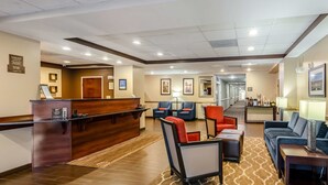 A hotel lobby with a reception desk, seating area, and a hallway leading to other rooms.