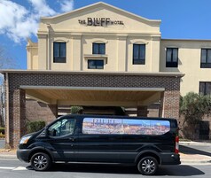 Una camioneta negra estacionada frente al Hotel The Bluff, con un anuncio de un paisaje urbano en su lateral.