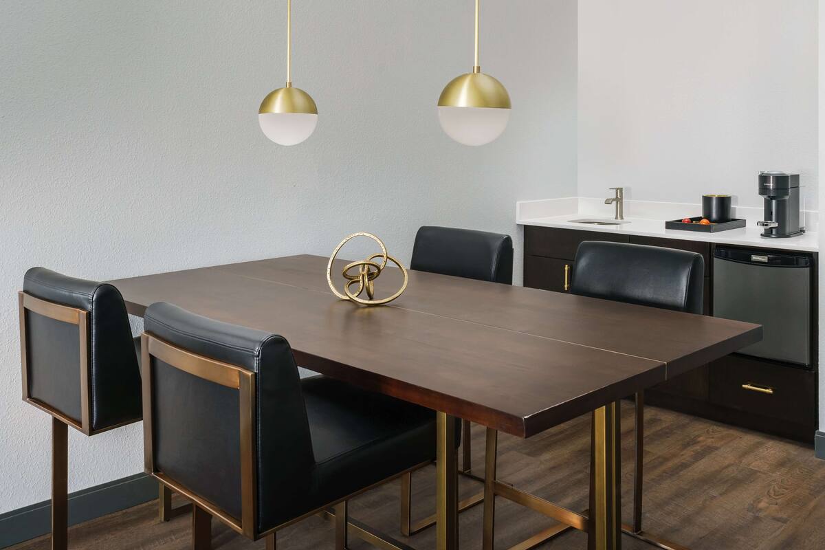 Un comedor moderno con una mesa de madera oscura, sillas de cuero negro y lámparas colgantes doradas y blancas.