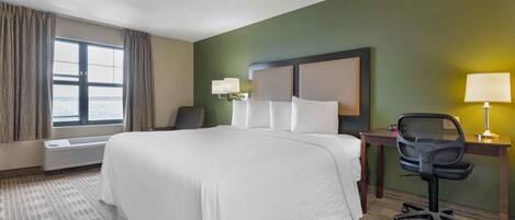 A hotel room with a large bed, a desk with a chair, a lamp, and a window with curtains.