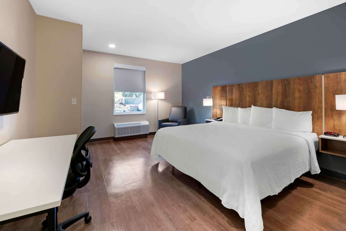 Une chambre d’hôtel avec un lit, un bureau, une chaise et un téléviseur fixé au mur.