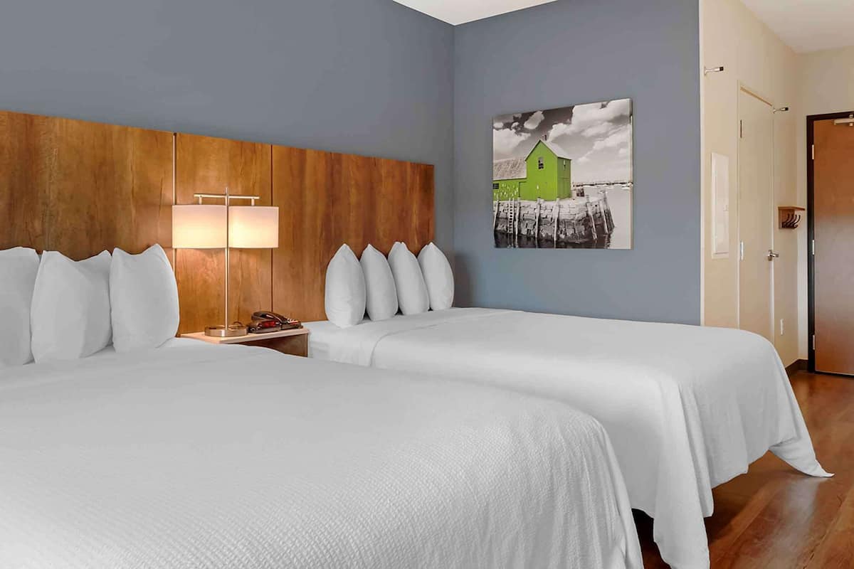 Une chambre d’hôtel avec deux lits, une tête de lit en bois, une table de chevet, une lampe et un tableau au mur.
