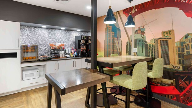 A modern kitchen with a cityscape mural, a dining area with chairs, and a coffee station.