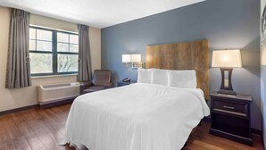A hotel room with a large bed, two bedside lamps, a wooden headboard, a chair, a nightstand, and a window with curtains.