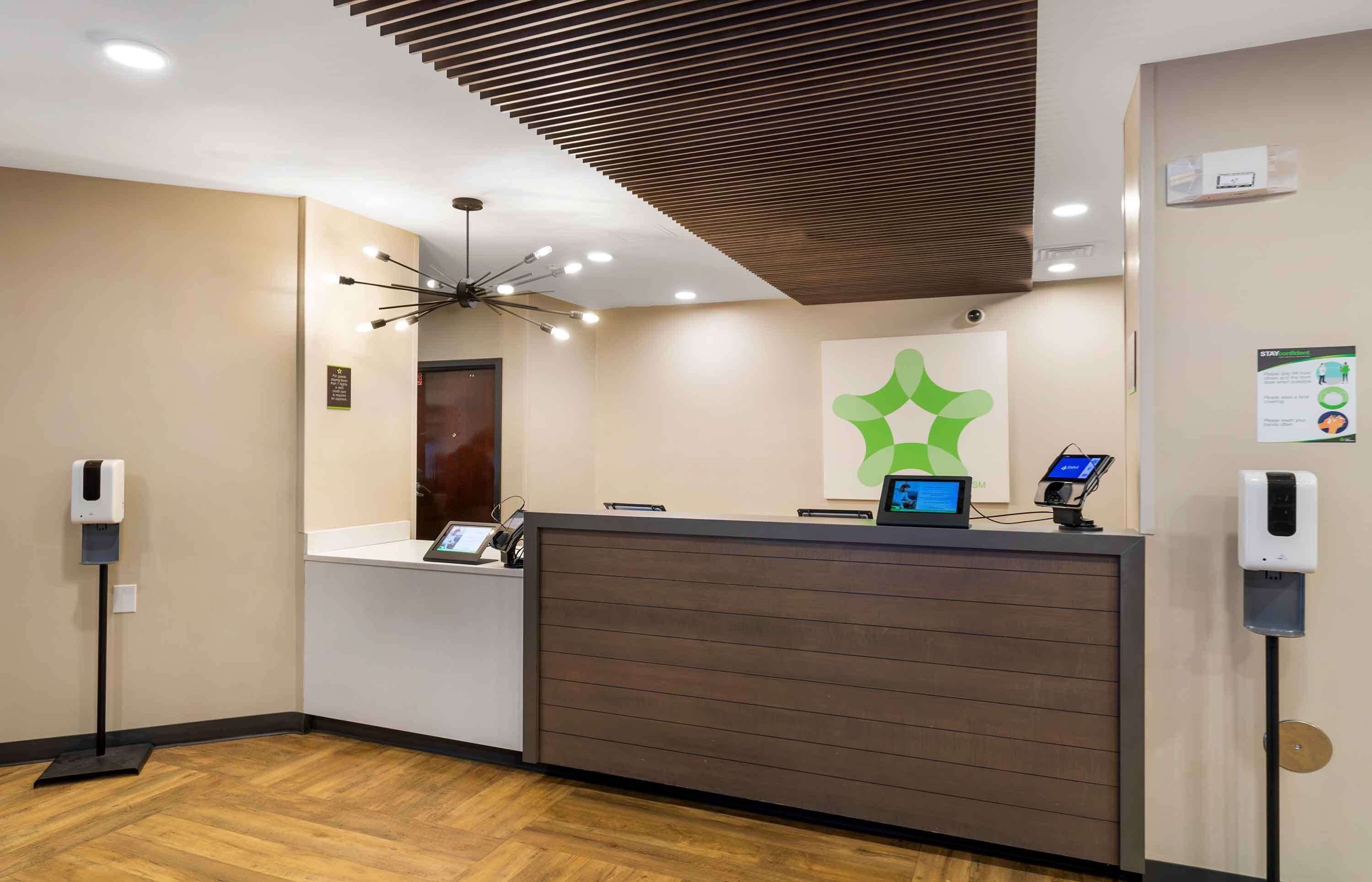 Een receptiezone met een modern design, met een receptiebalie, een digitaal scherm, een plafondlamp en een luchtzuiveraar aan de muur.