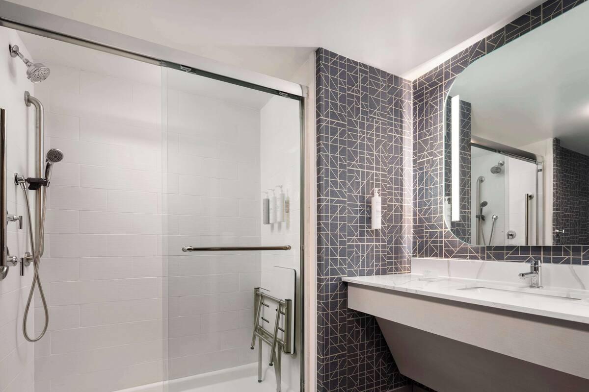 A modern bathroom with a glass-enclosed shower, a white sink, and a mirror with a geometric tile backsplash.