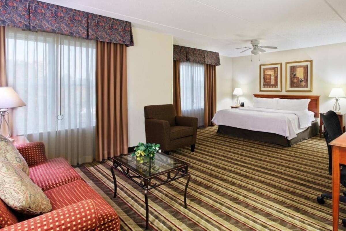 A hotel room with a bed, a sofa, a chair, a coffee table, and a desk.