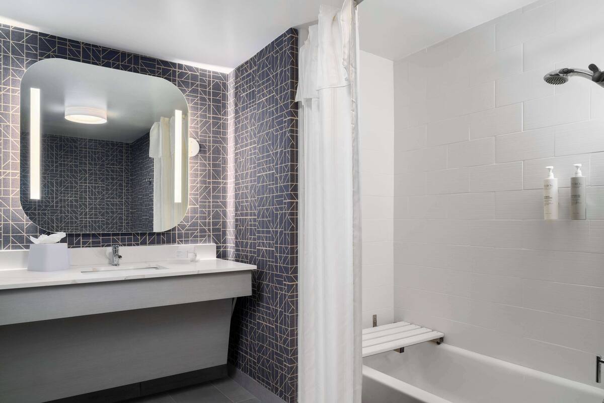 A modern bathroom with a white sink, a large mirror, and a shower area.