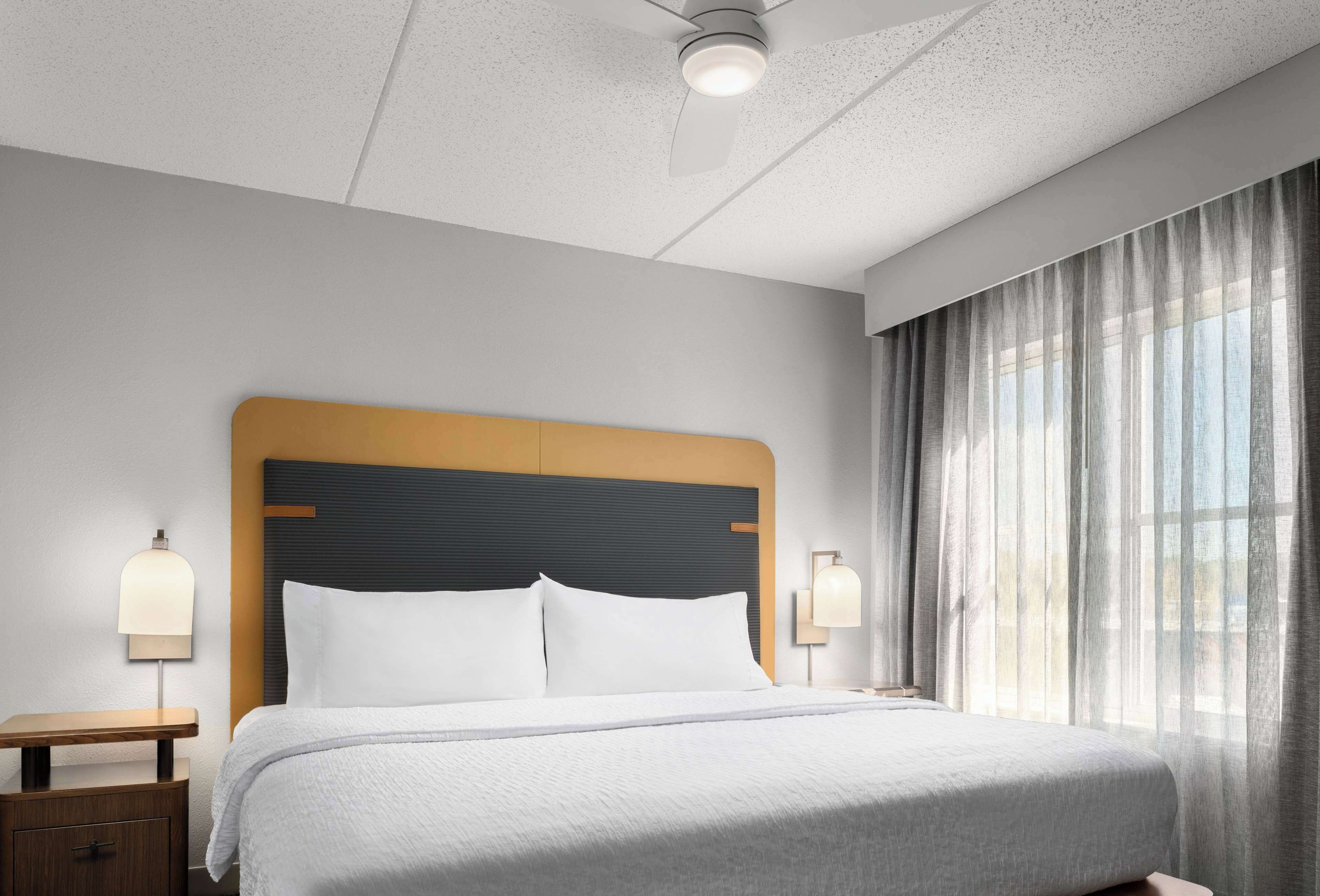Een hotelkamer met een bed, nachtkastjes, een plafondventilator en een raam met gordijnen.