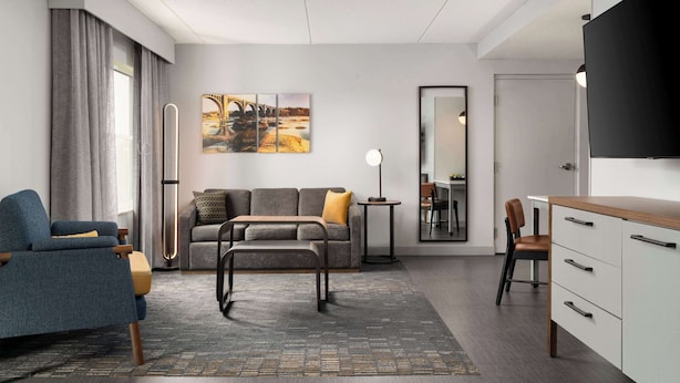 A modern hotel room with a sofa, a chair, a desk, and a flat-screen TV.