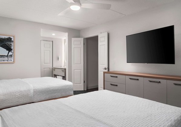 A hotel room with two beds, a flat-screen TV mounted on the wall, a wooden dresser, and a door leading to another room.