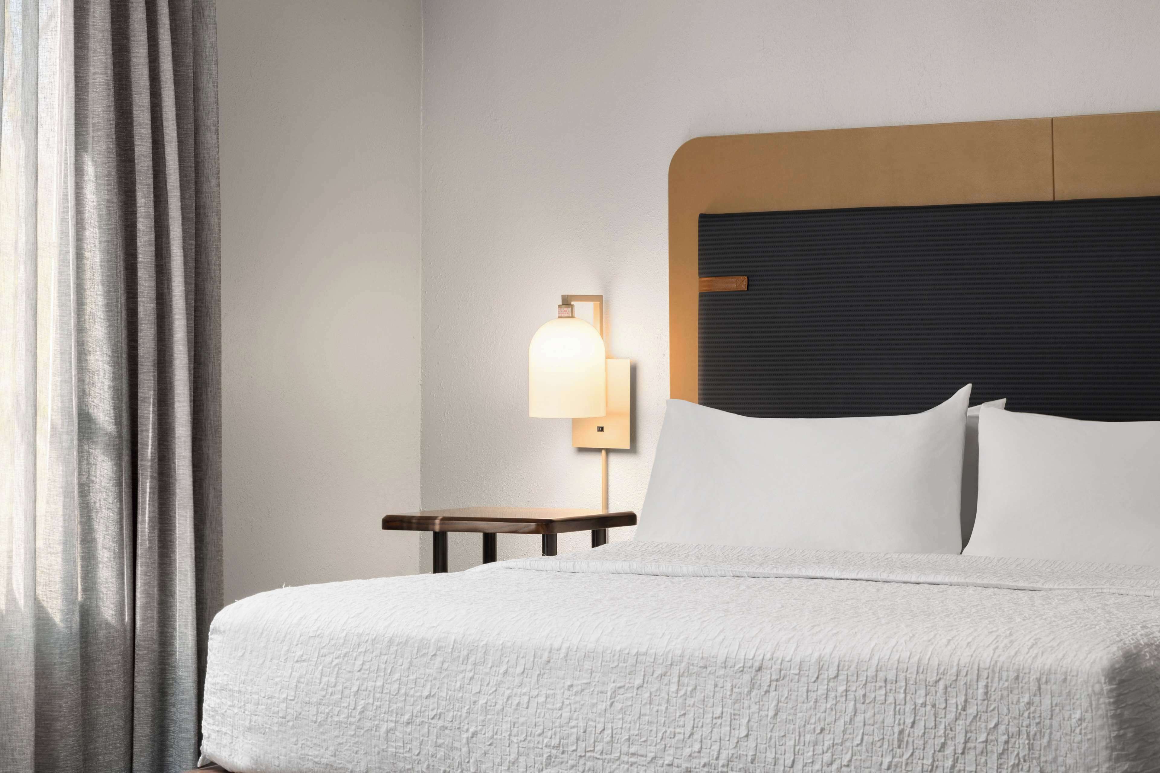 A neatly made bed with white linens, a wooden headboard, and a bedside table with a lamp.