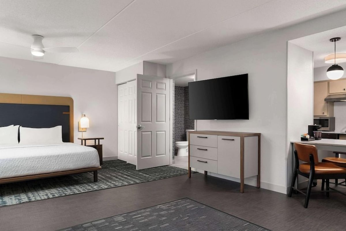 Una habitación de hotel moderna con cama, escritorio, televisor y baño.
