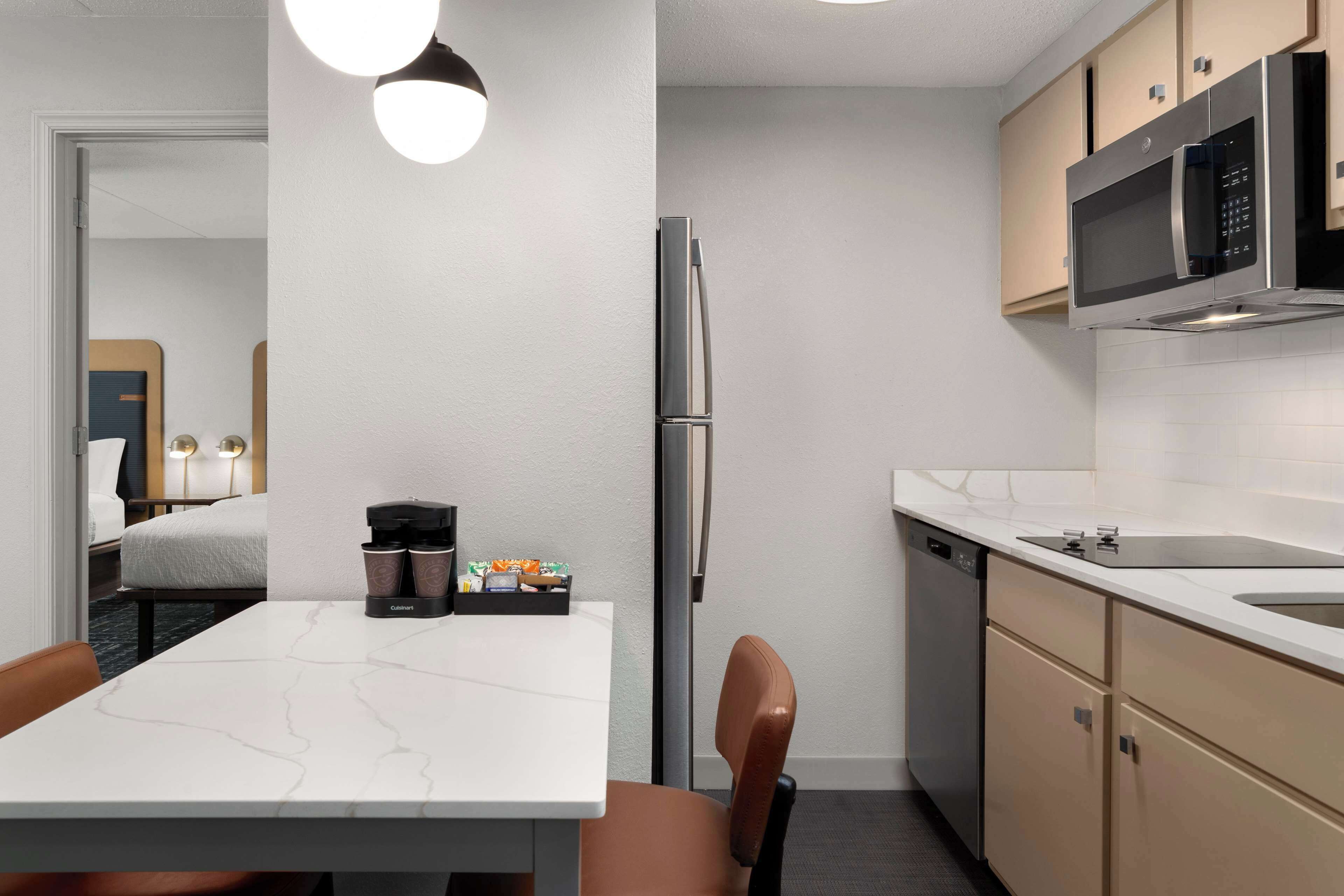 Una cocina moderna con un refrigerador de acero inoxidable, un microondas y un lavavajillas. Hay una encimera de mármol blanco y una mesa de comedor con dos sillas.
