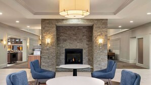 A modern hotel lobby with a stone fireplace, round tables, and blue armchairs.