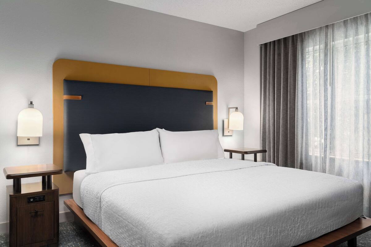 A neatly made bed with a headboard, bedside tables, and wall-mounted lamps.