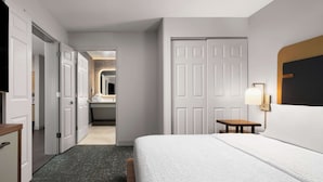 A hotel room with a bed, a desk, a chair, a TV, and a bathroom visible through an open door.