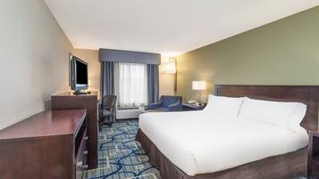 A hotel room with a large bed, a desk, a chair, a TV, and a window with curtains.