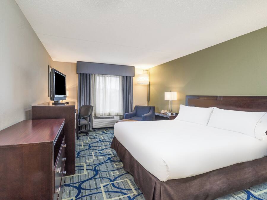 A hotel room with a large bed, a desk, a chair, a TV, and a window with curtains.