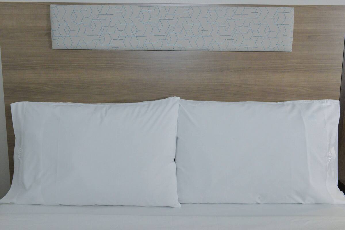 Una cama con dos almohadas blancas y un cabecero de madera.
