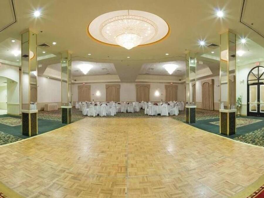 Un amplio salón con suelo de madera, paredes espejadas y un candelabro.