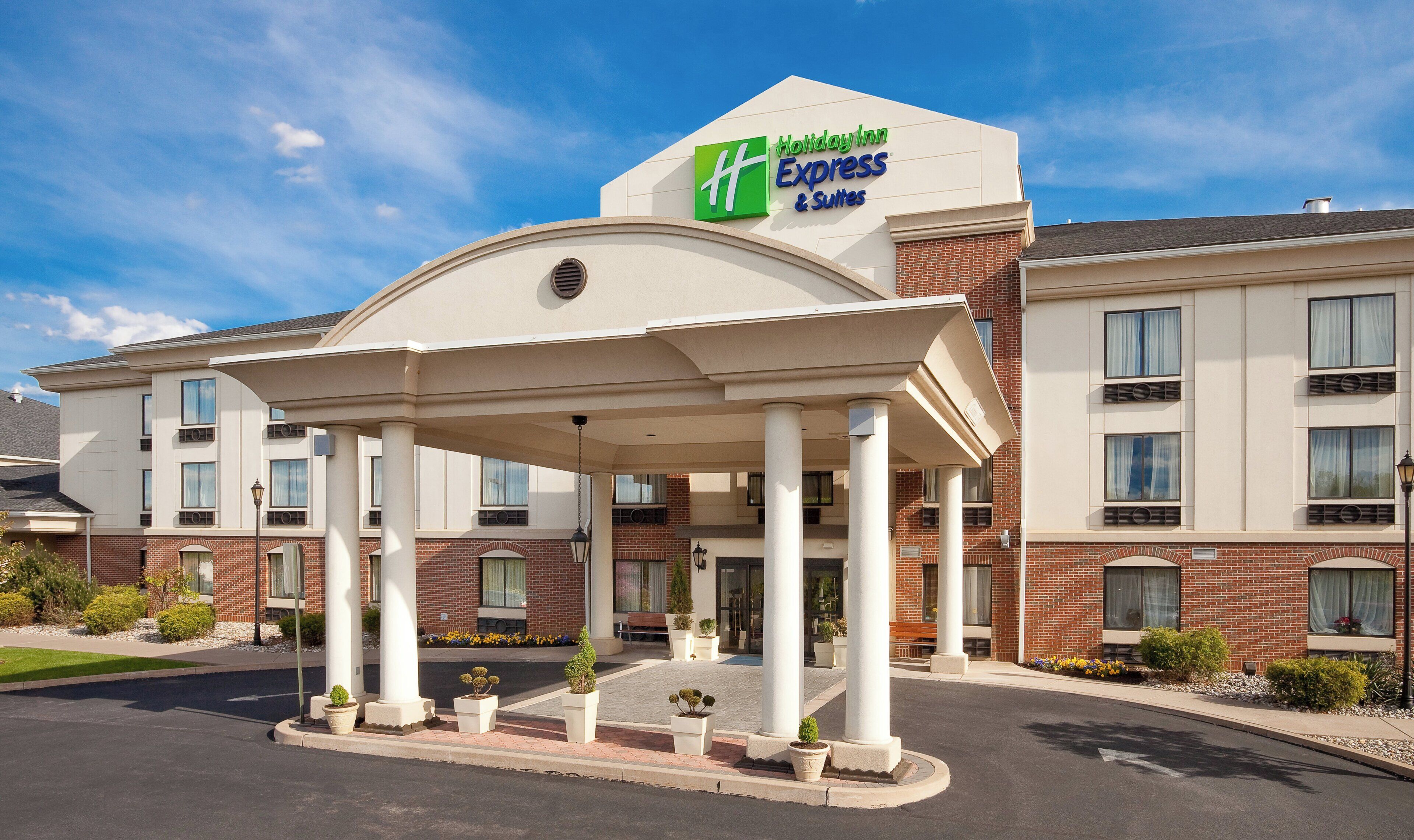 A Holiday Inn Express & Suites building with a covered entrance, multiple columns, and a brick facade.
