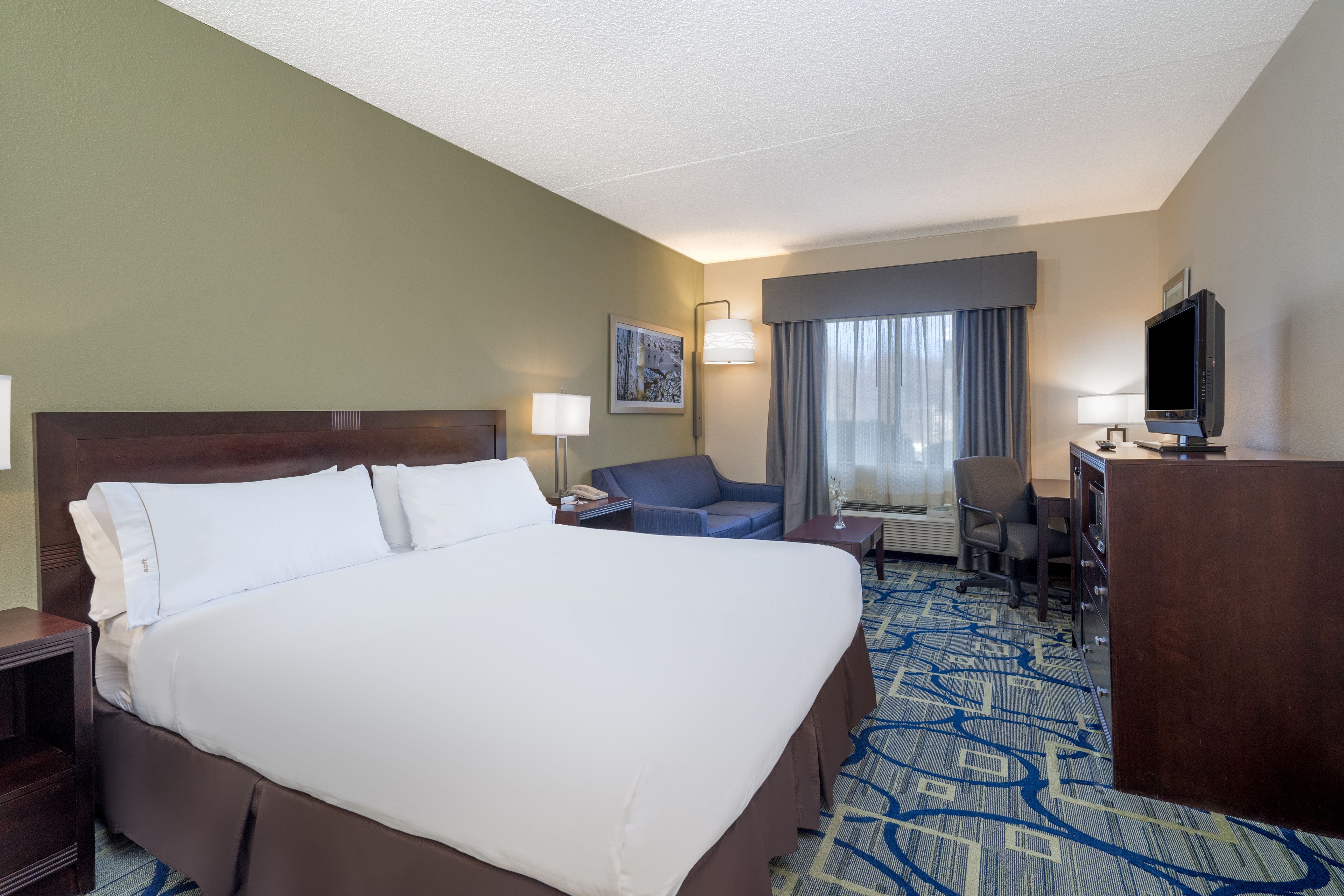 A hotel room with a large bed, a desk, a chair, a television, and a window with curtains.