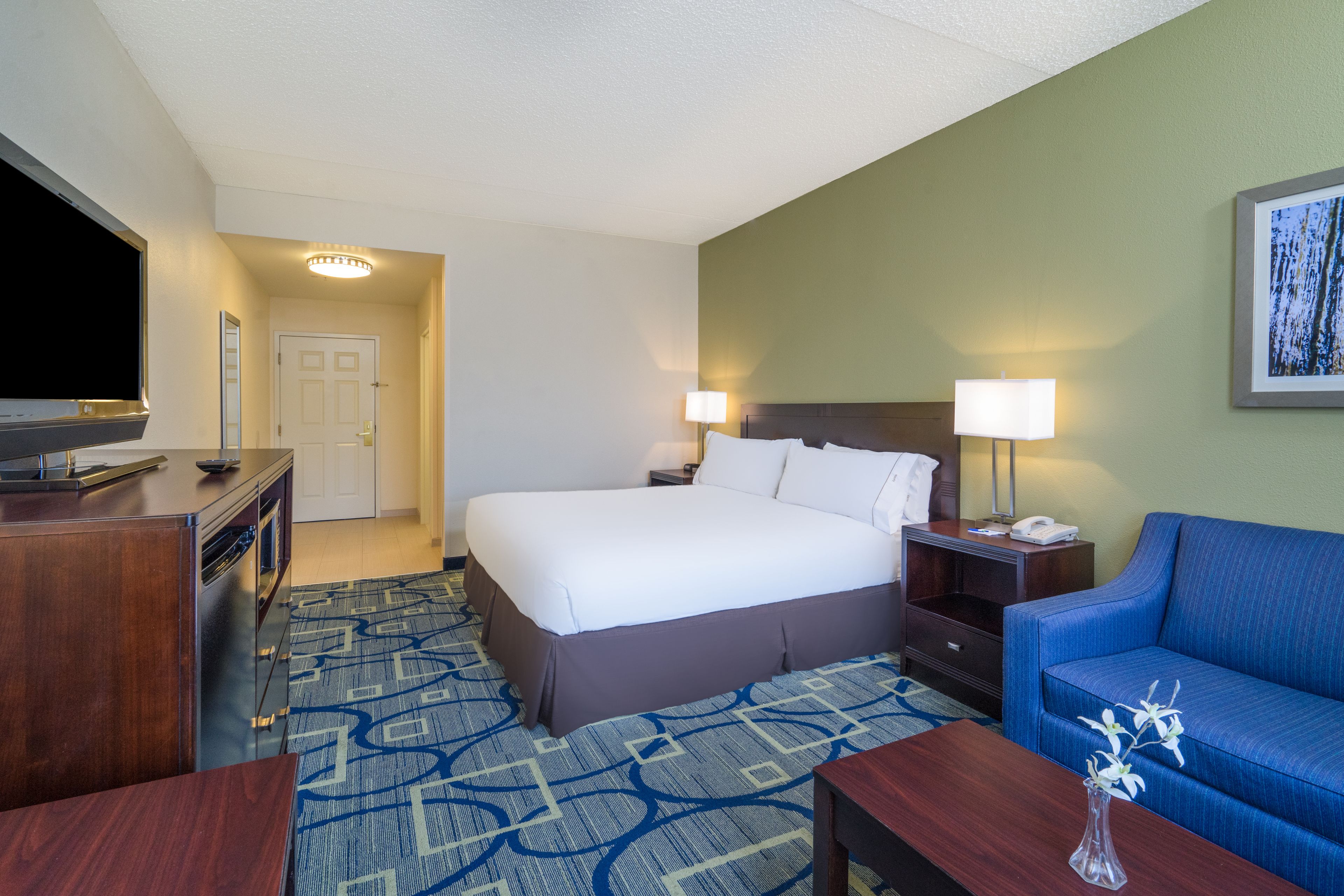 A hotel room with a large bed, a TV, a desk, a lamp, and a couch.