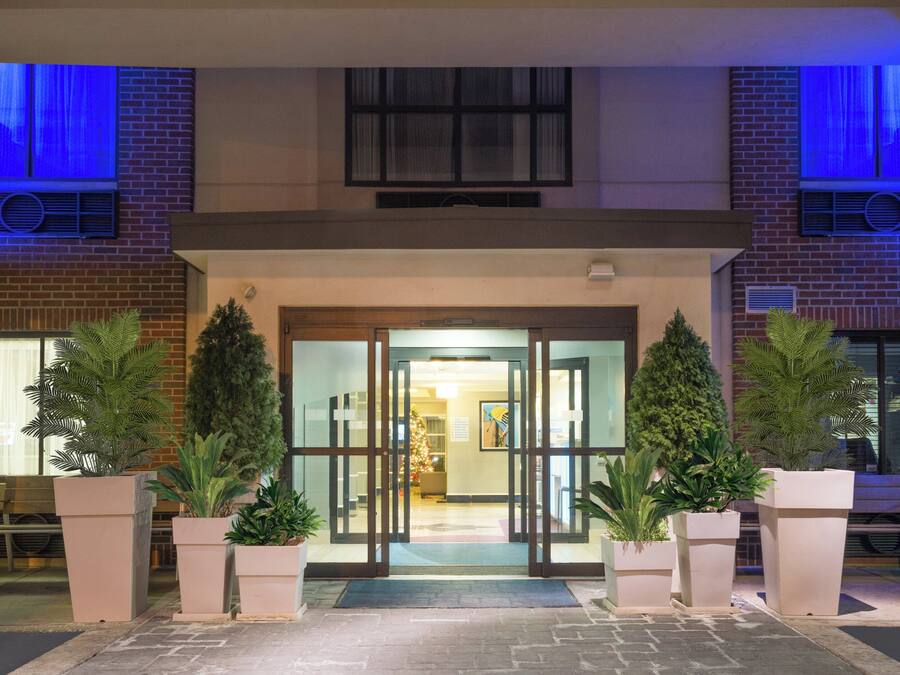 Entrada de hotel con puerta de cristal, plantas en macetas y fachada de ladrillo.