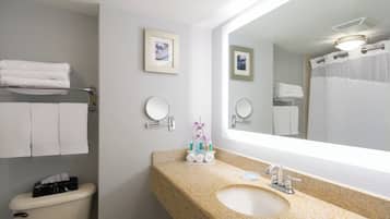 A bathroom with a toilet, sink, and two mirrors. There are towels on a rack and a shower curtain.