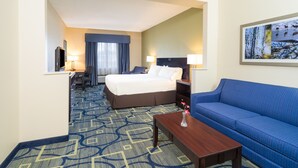 Habitación de hotel con una cama, un sofá azul, un escritorio y un televisor.