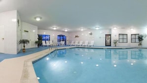 An indoor swimming pool with white lounge chairs and ceiling lights.